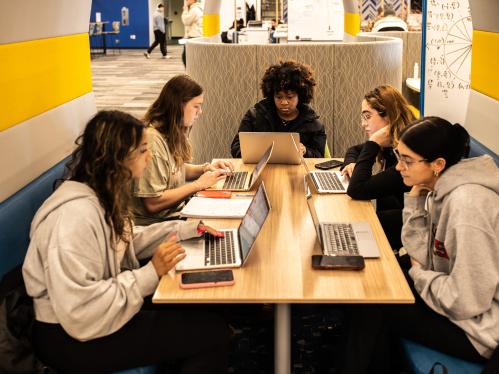 A picture taken of several students sitting around a table on their laptops