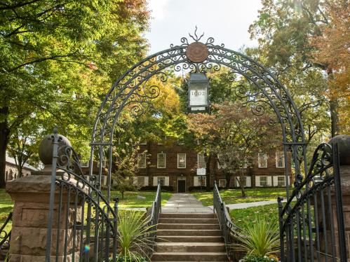 A picture taken of a gate at Rutgers leading to a university building. The gate has an arch with a lantern with the text "1902" on it.